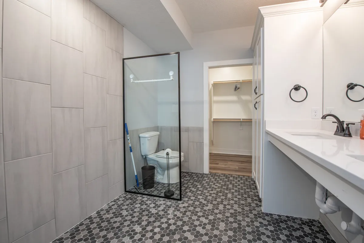 A bright, modern bathroom with a double sink vanity, glass shower enclosure, and stylish hexagonal floor tiles. The layout is open and accessible, emphasizing ease of movement and a fresh, inviting atmosphere.
