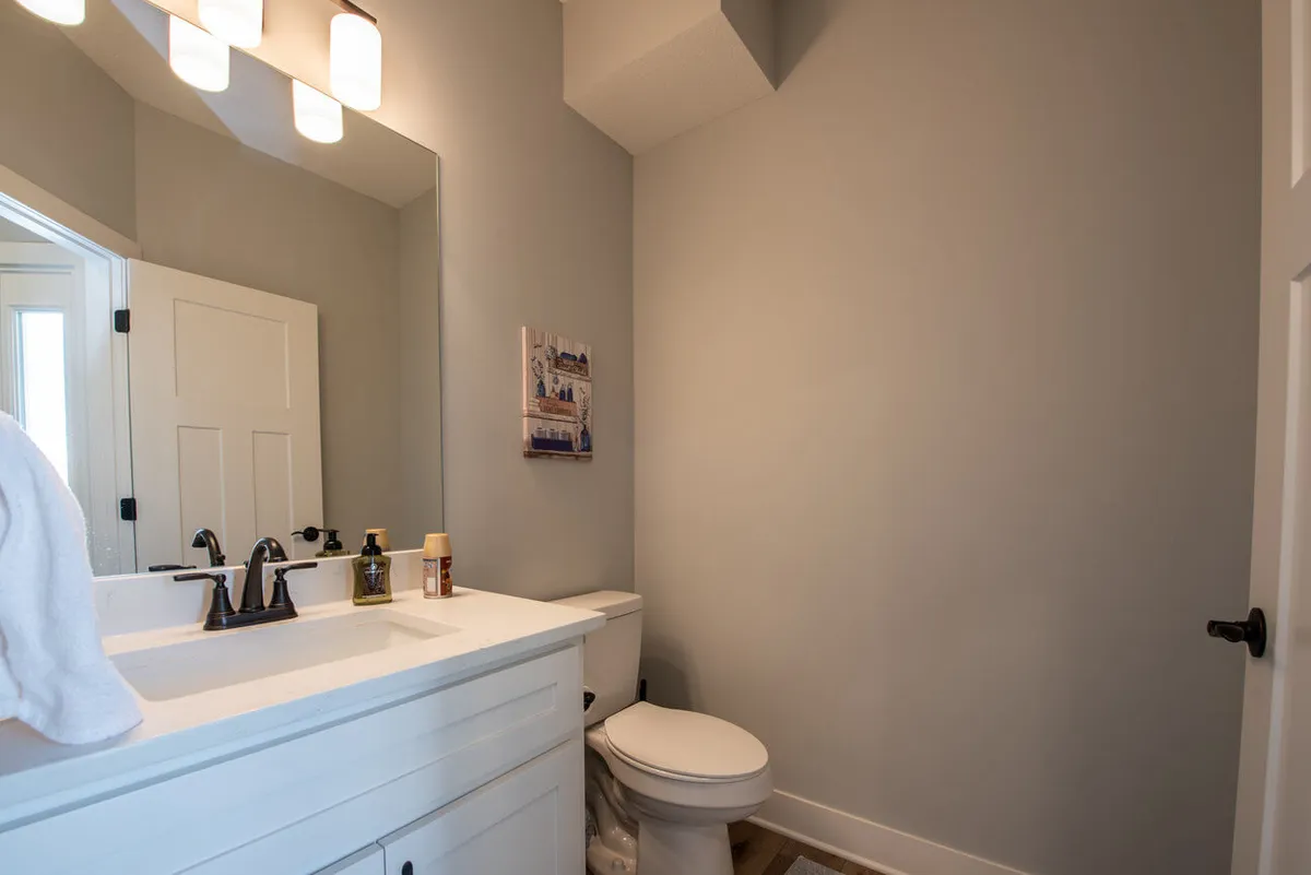 An inviting bathroom featuring a wide vanity with a large mirror, contemporary lighting, a toilet, and tasteful wall art. The space feels fresh and uncluttered, designed for easy morning routines or restful evening wind-downs.