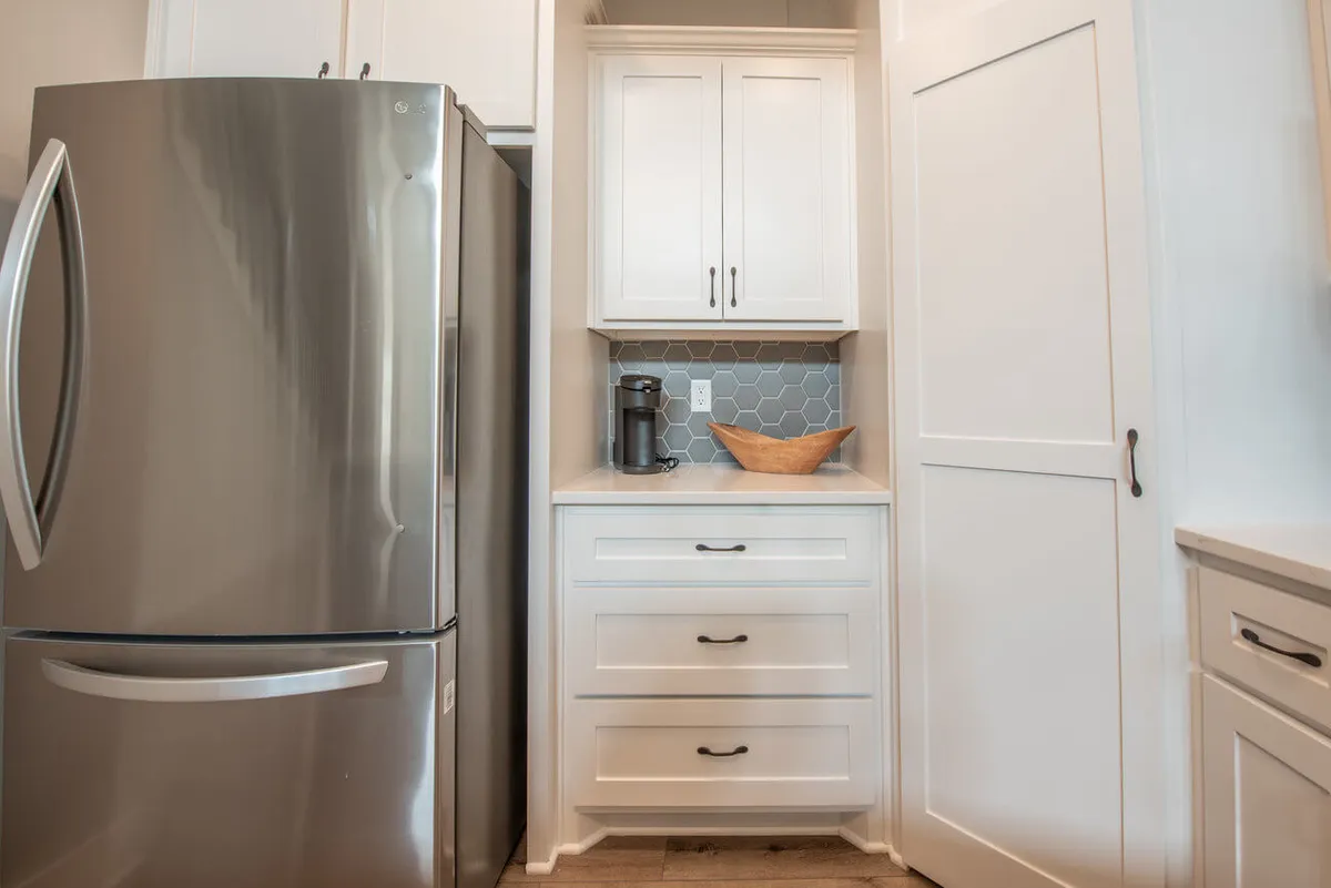 A modern kitchen with a stainless steel refrigerator, white cabinetry, a distinctive hexagonal backsplash, and a wooden bowl on the counter. The scene conveys a cozy space for preparing and sharing meals after a day out.
